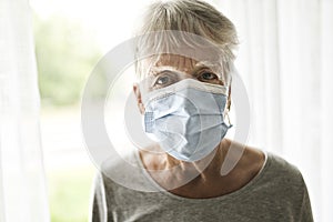 An elderly woman in a protective mask in front of window