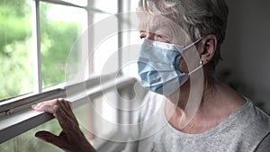 An elderly woman in a protective mask in front of window