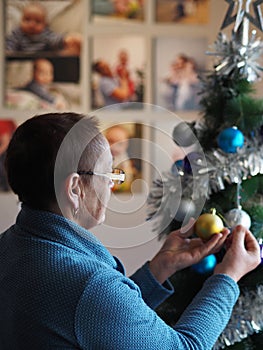An elderly woman in a protective medical mask decorates a Christmas tree during the coronavirus pandemic. The concept of