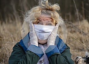 An elderly woman in a protective medical mask and rubber gloves holds her head