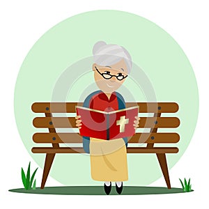 Elderly woman reads the Bible while sitting on a park bench.