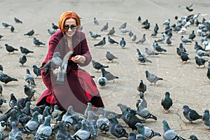 Elderly woman with red hair feeding pigeons in the park