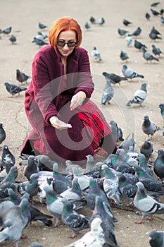 Elderly woman with red hair feeding pigeons in the park