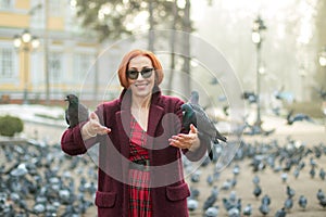 Elderly woman with red hair feeding pigeons in the park