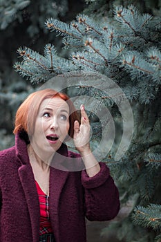 An elderly woman with red hair is surprised. A woman stands next to a blue spruce