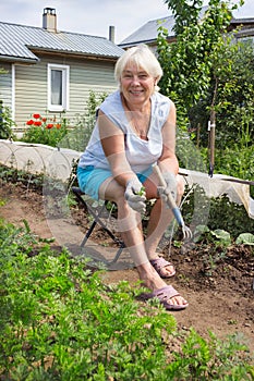 Elderly woman removes the weeds in the garden