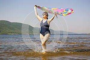 elderly woman runs along the waves on a summer sunny day against the background of mountains