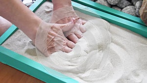 Elderly woman`s hands digging in the sand in a box