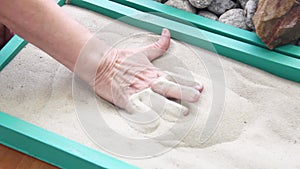 Elderly woman`s hands digging in the sand in a box