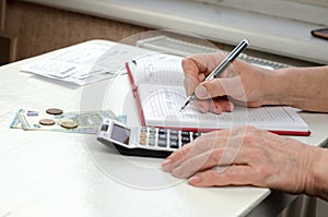 An elderly woman`s hands holding a pen working on a utility bill calculator