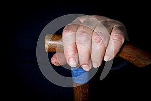 Elderly woman`s hands on an old walking stick with t shaped handles. The concept of old age, loneliness, solicitude