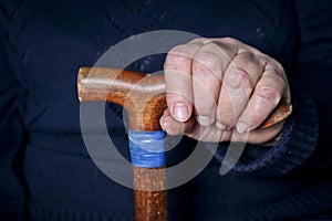 Elderly woman`s hands on an old walking stick with t shaped handles. The concept of old age, loneliness, solicitude and caring photo