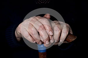 Elderly woman`s hands on an old walking stick with t shaped handles. The concept of old age, loneliness, solicitude and caring