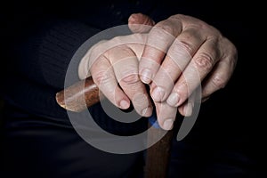 Elderly woman`s hands on an old walking stick with t shaped handles. The concept of old age, loneliness, solicitude and caring photo