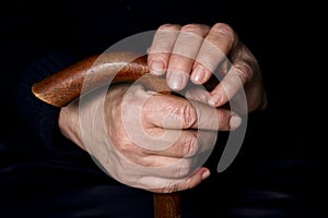 Elderly woman`s hands on an old walking stick with t shaped handles. The concept of old age, loneliness, solicitude and caring