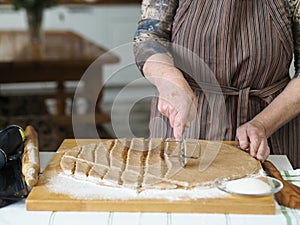 An elderly woman is hands roll out the dough and cut out cookies for baking in the oven with a special knife. The process of home