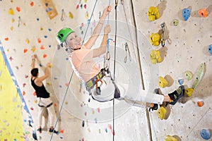 elderly woman in safety helmet and with safety rope hangs near climbing wall in gym