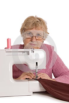 The elderly woman sews on the sewing machine