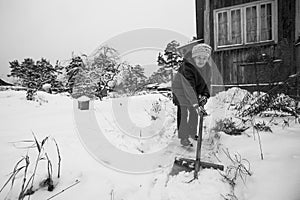 An elderly woman is shoveling snow outside her rural home. Black and white photo.