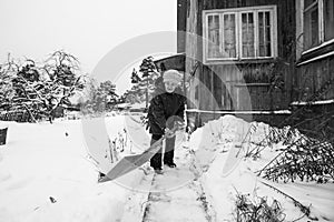 An elderly woman is shoveling snow outside her rural home. Black and white photo.