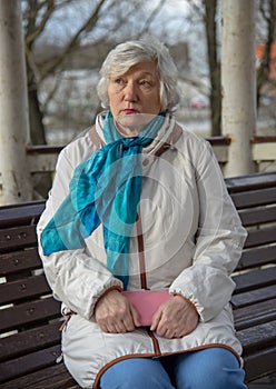 An elderly woman is sitting on a bench with a pink purse in her hands