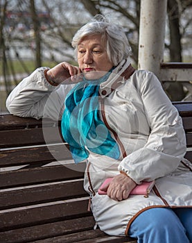 An elderly woman is sitting on a bench with a pink purse in her hands