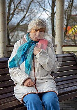 An elderly woman is sitting on a bench with a pink purse in her hands .