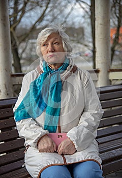 An elderly woman is sitting on a bench with a pink purse in her hands .