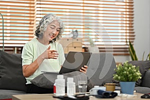 Elderly woman sitting on couch having online consultation with doctor on laptop. Telehealth consultation, tele medicine
