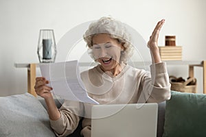 Elderly woman sitting on couch reading paper letter feels overjoyed