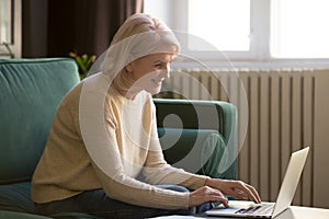 Elderly woman sitting on couch typing on computer