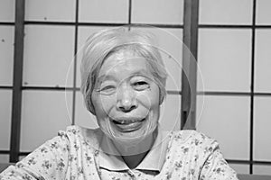 Elderly woman sitting down in front of shoji screen smiling