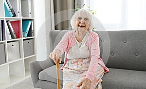 Elderly Woman Sitting On A Living Room Sofa Laughing And Looking Into The Camera