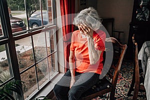  elderly woman sitting near the window at her home with her head in her hand