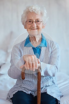 Elderly woman, sitting portrait and smile on bed with happiness, walking stick and relax in nursing home. Happy senior