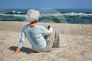 Elderly woman sitting in the sand on the beach sea