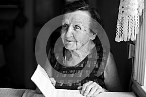 An elderly woman sitting at table in the house. Black and white photo.