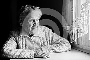 Elderly woman sitting at a table near the window.