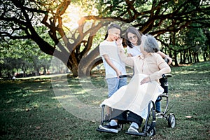 Elderly woman sitting in a wheelchair, smiling and happy with her daughter and grandson taking care of her