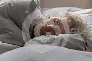 Elderly woman sleeping in bed under blanket in cozy bedroom