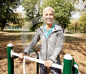 Elderly Woman In Sports Clothes Exercising At Outdoor Fitness Park