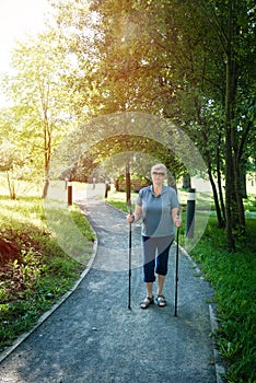 Elderly woman standing on footpath with Nordic walking poles