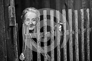 An elderly woman stands behind a wooden fence in the village