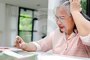 An elderly woman stressed about her finances is debiting her credit card.