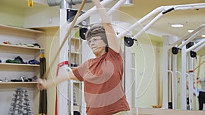 Elderly woman stretching out, doing tilt exercises with stick in fitness room. Healthy gymnastics. Active seniors.