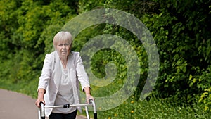 Elderly woman strolling with walker on path lined with trees and grass