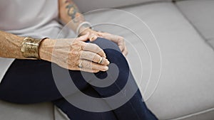 Elderly woman suffering tremendous knee pain, adult, resting despondently in the comfort of her living room sofa, glancing at her