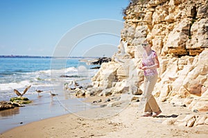 Elderly woman in sunglasses feeds seagulls on the beach