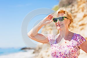 Elderly woman in sunglasses looking at the sea and having fan.
