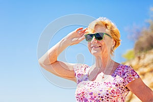 Elderly woman in sunglasses looking at the sea and having fun.